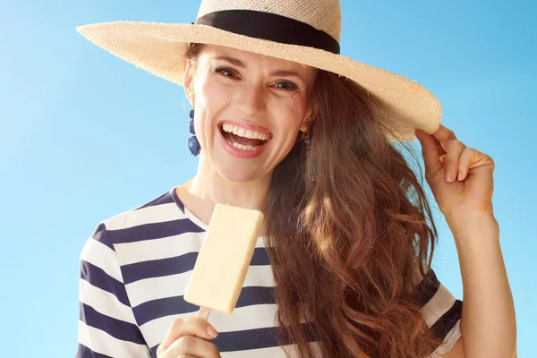 愉快的年轻妇女在草帽反对蓝色天空吃冰淇淋 — 图库照片