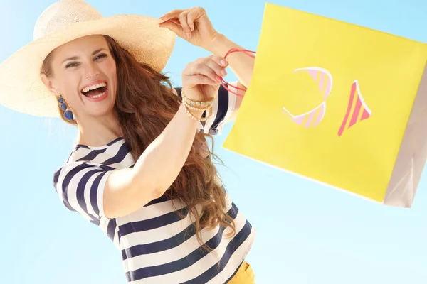 麦わら帽子ビキニで黄色の買い物袋と青い空を背景に陽気なトレンディな女性 — ストック写真