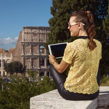 arkadan görünüşü parapetin üzerinde oturan ve tablet Pc yakınlarında Kolezyum, Roma, İtalya, kullanma trendy turist kadın  