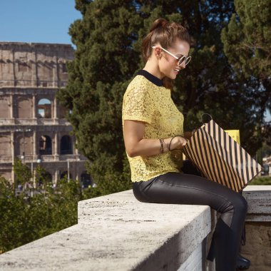 mutlu şık turist kadın sarı bluz parapet yakınlarında Kolezyum, Roma, İtalya, otururken alışveriş çantası arıyorsunuz
