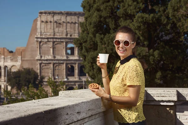 happy young tourist woman in yellow blouse with coffee and Italian mini crostata posing near Colosseum , Rome, Italy
