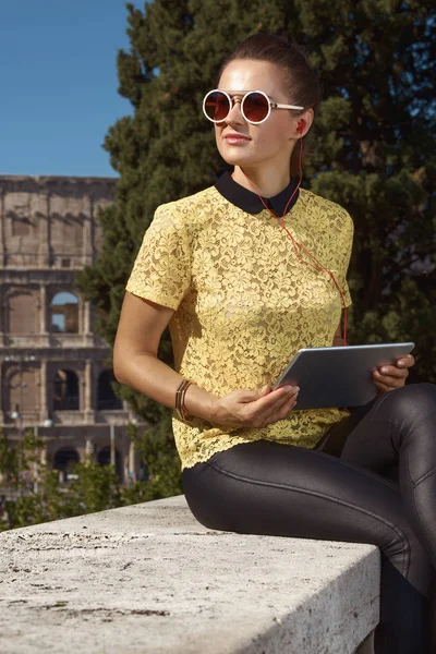stylish tourist woman in yellow blouse listening to audio guide on tablet PC near Colosseum , Rome, Italy
