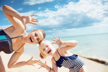 Modern anne ve kızı boş avuç içi sahil üzerinde gösterilen mayo gülümseyen