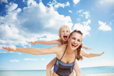 Modern anne onun kızı piggy geri vererek gülümseyen portresi binmek sahil üzerinde