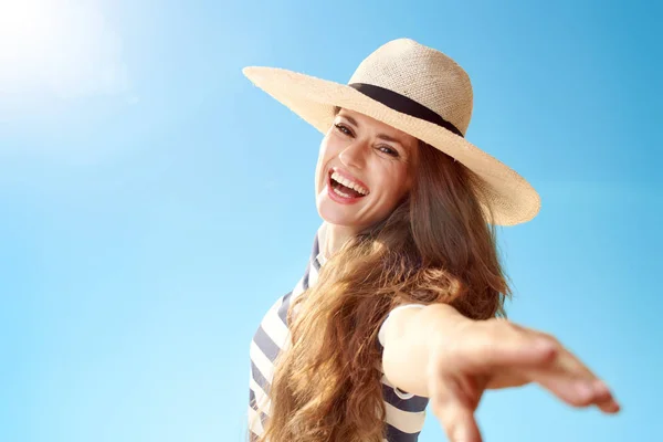 Portrait of smiling trendy woman in straw hat having fun time against blue sky