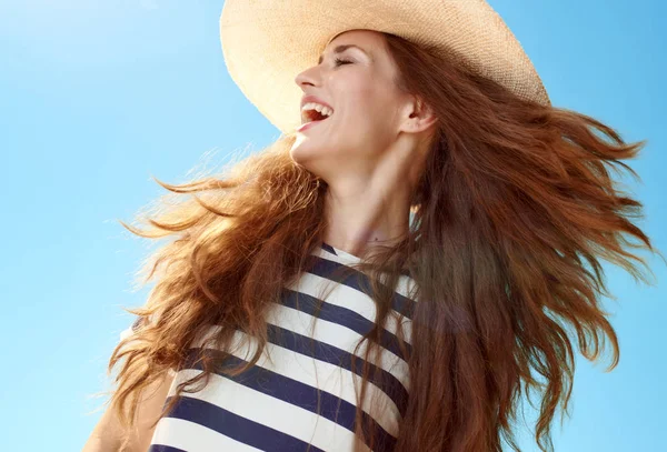 时髦的妇女在草帽与飘扬的头发看一边对蓝色天空 — 图库照片
