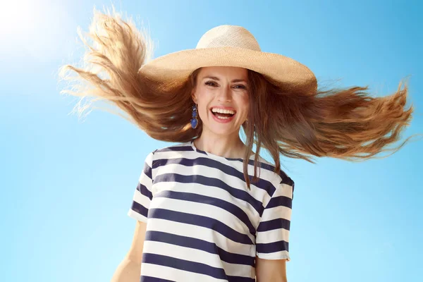 happy modern woman in straw hat with fluttering hair against blue sky