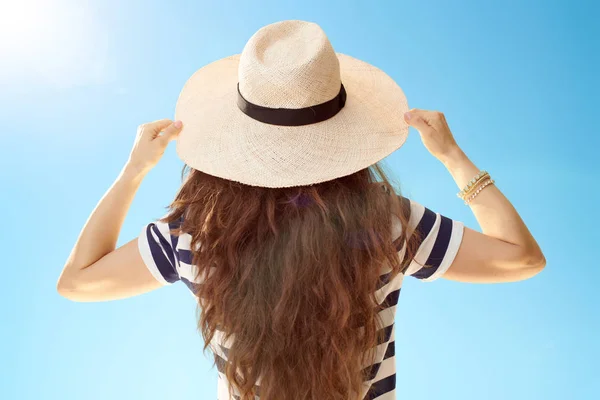 青空麦わら帽子に長いブルネットの髪を持つトレンディな女性の背面図 — ストック写真