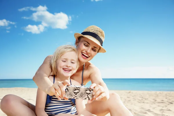 幸せな若い母と娘水着ビーチでスマート フォンで Selfie を取って — ストック写真