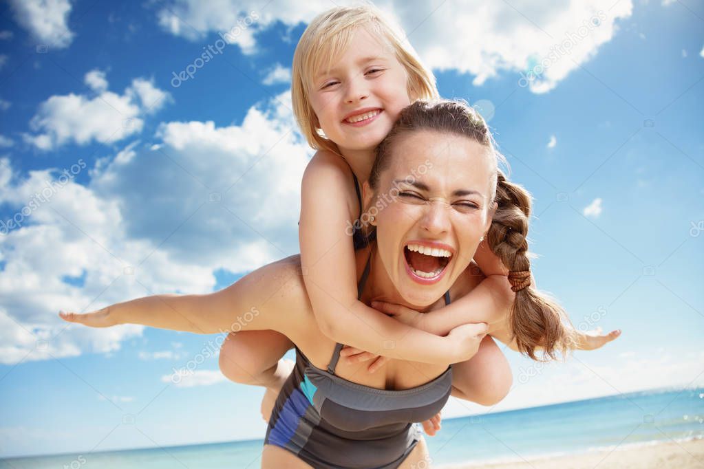 happy young mother mother giving her daughter piggy back ride at seacoast 