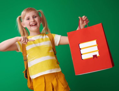 liseli kız alışveriş çantası ile yeşil arka plan ileti örneğine işaret sırt çantası ile gülümseyen