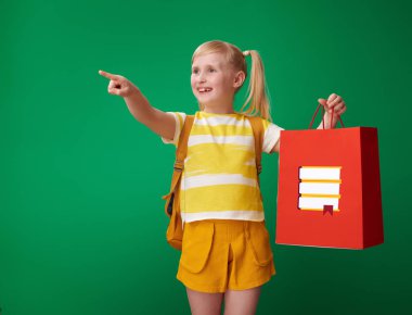 alışveriş çantası ileti örneği ile tutarak ve ileriye dönük yeşil arka plan üzerinde sırt çantası ile öğrenci gülümseyen