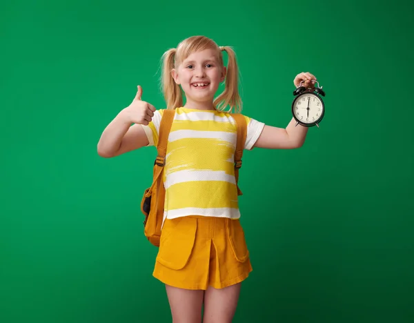 Chica Escuela Feliz Con Mochila Con Reloj Despertador Mostrando Pulgar —  Fotos de Stock