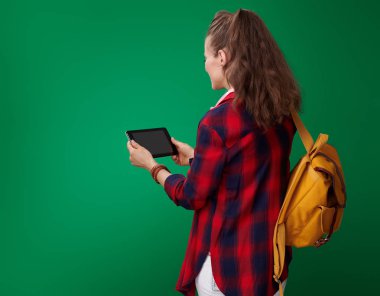 arkadan görünüşü genç öğrenci kadın sırt çantası ve tablet Pc yeşil arka plana karşı kullanma kulaklıklar ile kırmızı gömlekli
