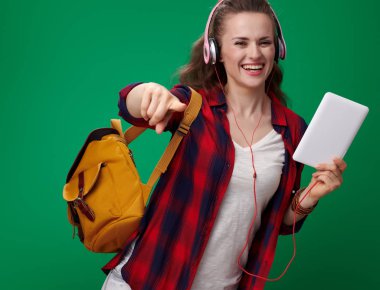 sırt çantası ve tablet Pc tutarak ve kamera yeşil arka planı gösteren kulaklık ile kırmızı gömlek gülümseyen modern öğrenci kadın