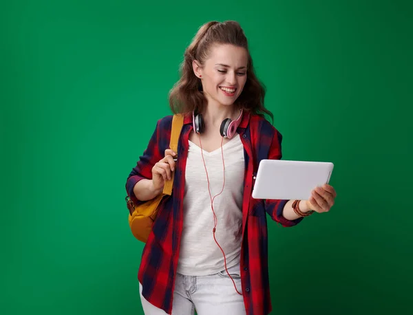 バックパックと緑の背景にタブレット を使用するヘッドフォンと赤シャツの笑顔の若い学生女性 — ストック写真