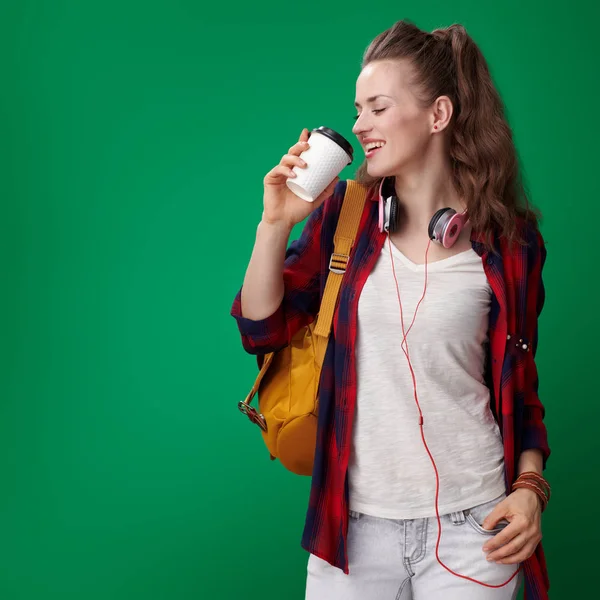 バックパックとヘッドフォン緑の背景にコーヒーを飲むと赤いシャツで幸せな若い学生女性 — ストック写真
