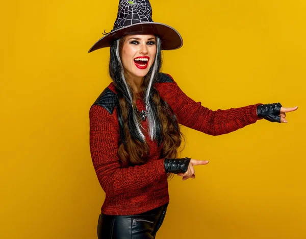 Sorrindo Mulher Moderna Traje Bruxa Halloween Apontando Lado Fundo Amarelo — Fotografia de Stock