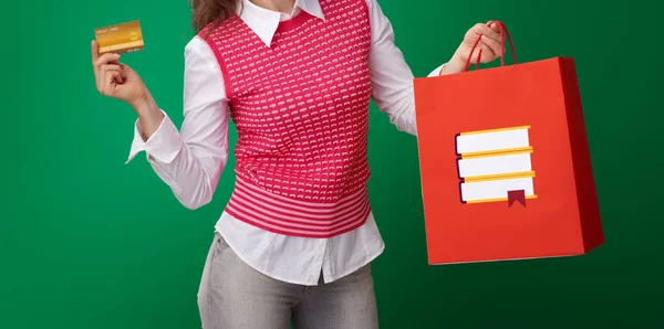 緑の背景の本とクレジット カードとショッピング バッグを示す赤のチョッキでモダンな学生女性 — ストック写真