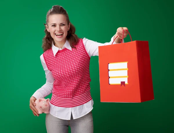 貯金本ショッピング バッグを与えて 緑背景貯金を押し赤いチョッキに笑顔のモダンな学生女性 — ストック写真
