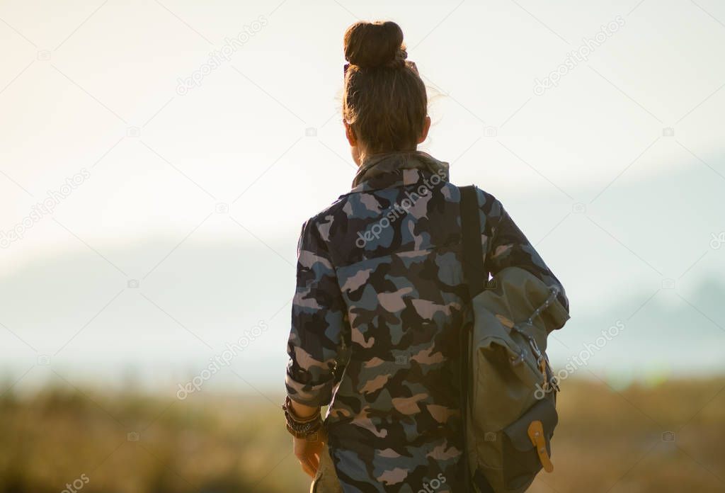 back view of tourist woman in hiking gear against mountain and ocean landscape at sunset