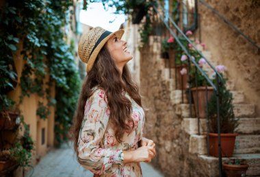 modern turist kadın uzun elbiseli ve hasır şapka gezi eski İtalyan kasabasında gülümseyen 