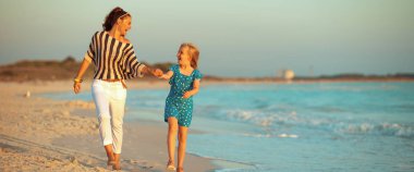 Modern anne ve sahil üzerinde günbatımında yürüyüş çocuk gülümseyen 