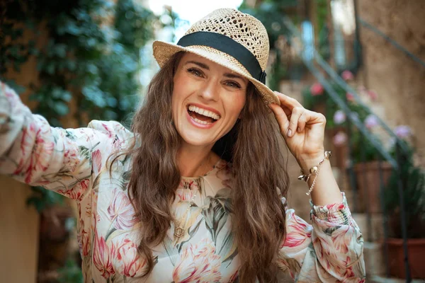 ドレスと古いヨーロッパの通りで楽しみながら笑っている麦わら帽子を身に着けている魅力的な観光女性 — ストック写真