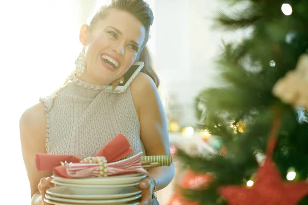 クリスマス ツリー近くのスマート フォンで話しているプレートを提供して笑顔のトレンディな主婦 — ストック写真