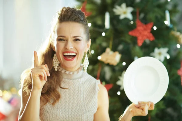 微笑的现代妇女附近的圣诞树举行服务白色餐盘和显示想法的标志 — 图库照片