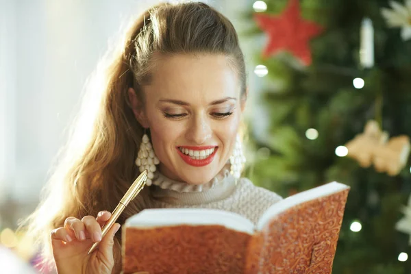 Lachende Moderne Huisvrouw Met Notebook Pen Buurt Van Kerstboom — Stockfoto