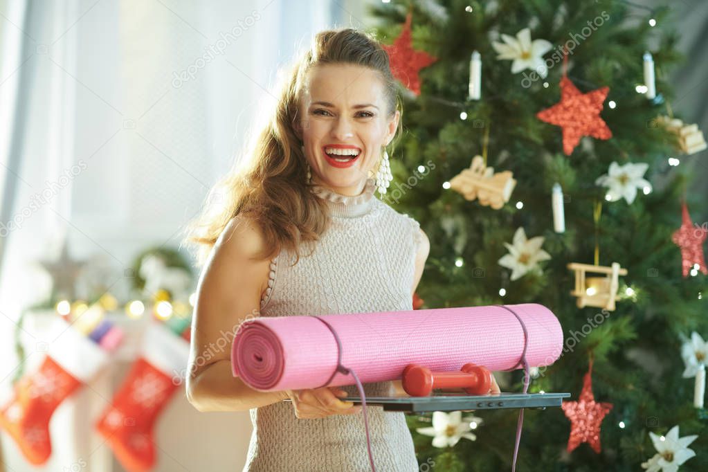 smiling trendy housewife with fitness gear near Christmas tree