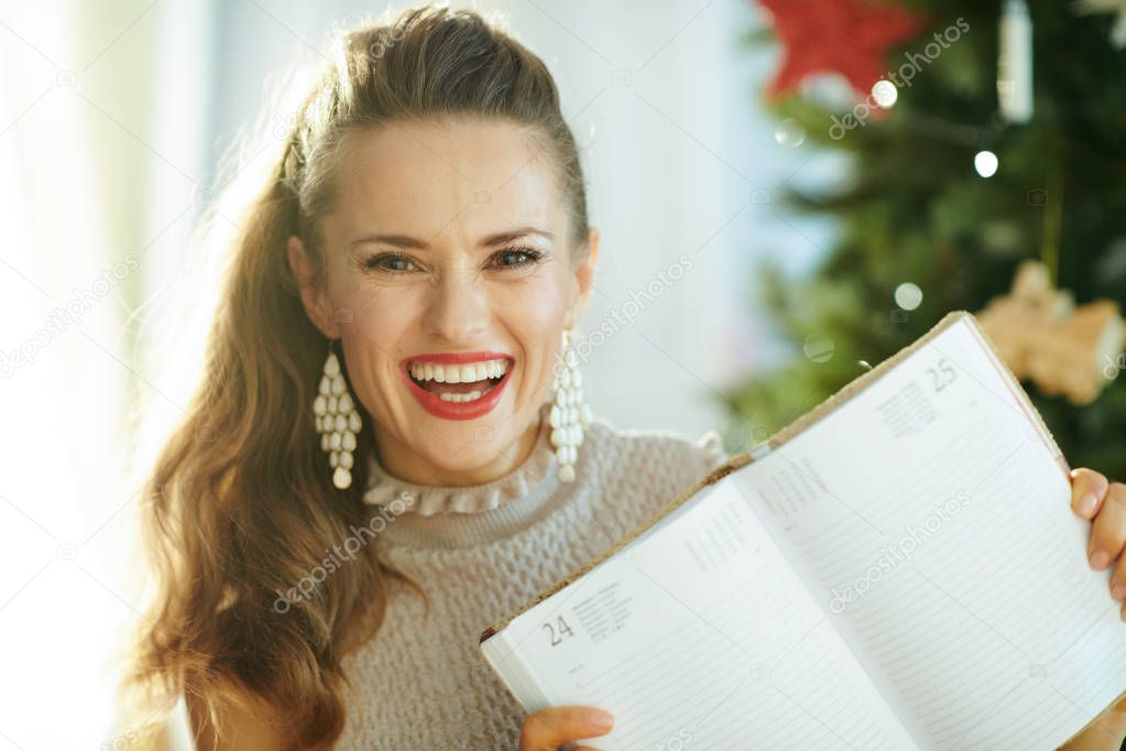 happy trendy housewife near Christmas tree showing diary on page December 25