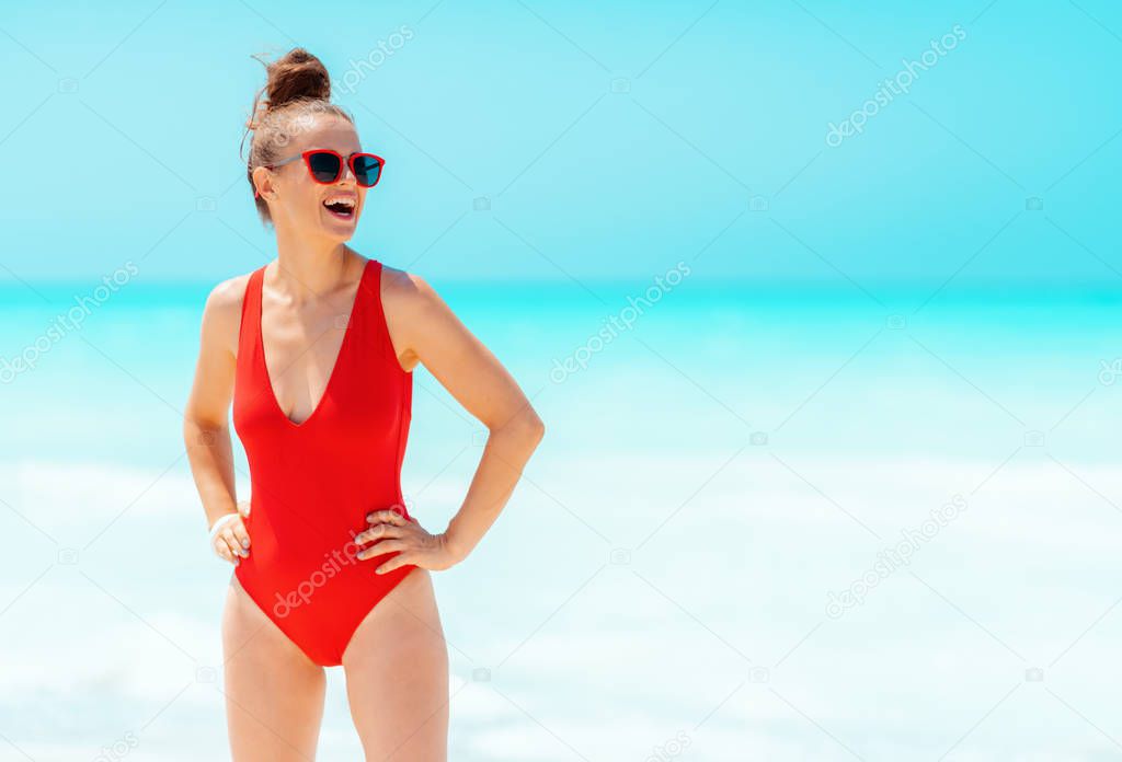 happy modern woman in red swimwear and glasses looking into distance on seacoast 