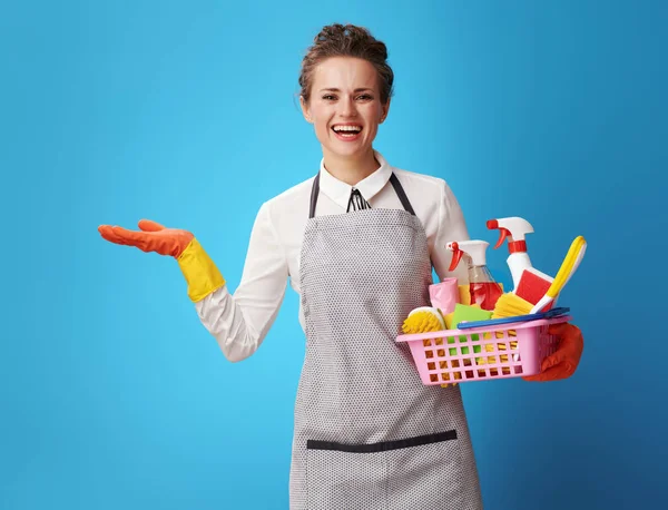 Smiling Young Housemaid Apron Basket Detergents Brushes Presenting Something Empty — Stock Photo, Image