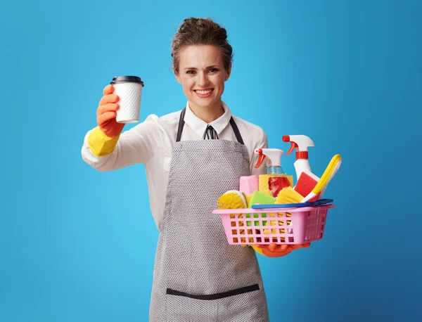 Smiling Young Housemaid Apron Basket Cleansers Brushes Giving Coffee Cup — Stock Photo, Image