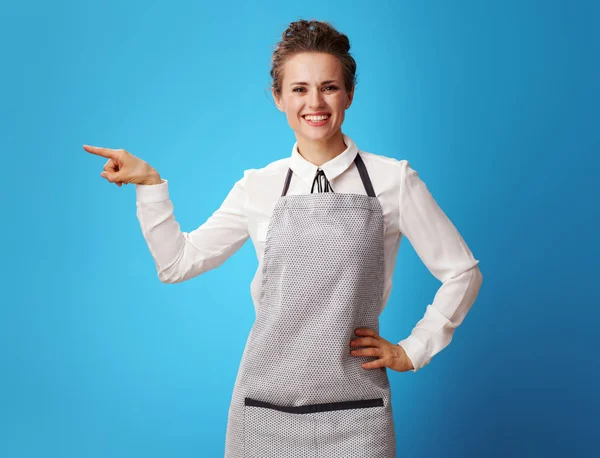 Glimlachend Jonge Schoonmaakster Schort Wijzend Iets Geïsoleerd Blauw Waar Vind — Stockfoto