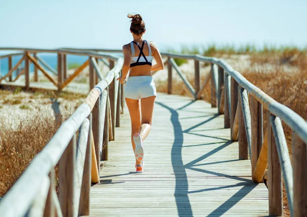 后面的年轻运动女子在海岸上跑步的健身服 — 图库照片