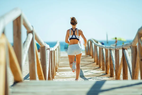 back view of woman jogger in fitness clothes jogging on wooden walkway at beach