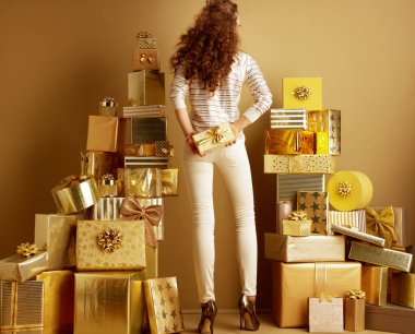 Modern kadın altın bej renkli giysiler 2 hediye kutusu tutarak düz bir duvar önünde altın hediye yığınları arasında arkasından gördüm. reklam Alışveriş Merkezi, Market, alışveriş merkezi. doğum günü illüstrasyon.