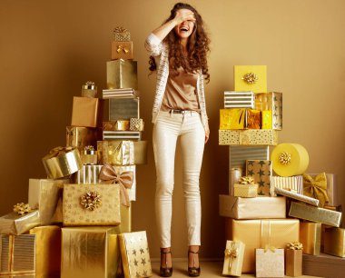 Bej giysili heyecanlı zarif kadın portresi tam uzunlukta el ve düz duvar önünde altın hediye yığını arasında dururken Gülen gözler kapalı 