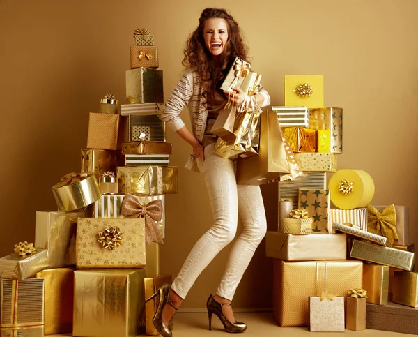 在一个普通的墙前 在一个普通的墙壁前 有两堆金色的礼物 上面有一个穿着金色米色衣服的快乐年轻时尚歌手的全长画像 假日购物例证 — 图库照片