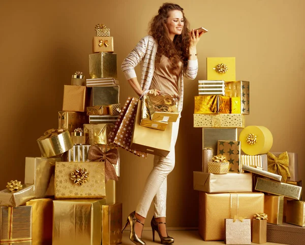 ses aramak yığın altın hediyeler arasında dururken ürün almak için smartphone uygulaması kullanarak altın alışveriş torbaları ile bej giysileri moda kadın