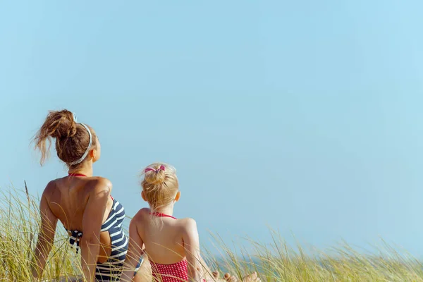 距離を探して海岸のビーチウェアは若い母と子の後ろから見られます 青い空 緑の草とは人々 と野生のビーチ 静かな休暇の天国 モダンなヨーロッパの母 — ストック写真