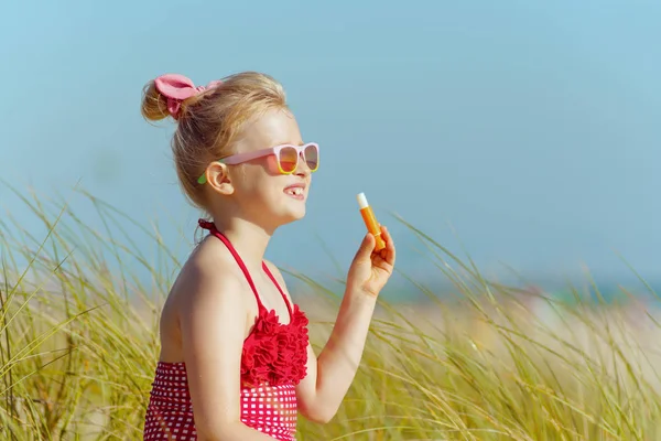 オーシャン ショアの Spf との口紅を持ちながら距離を探している赤い水着でトレンディな子 日当たりの良い夏の正午 — ストック写真