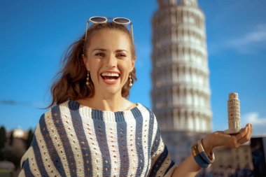 Leaning tower of Pisa Hatıra gösterilen gülümseyen zarif kadın çizgili bluz ön tarafında yaslanmış kule Pisa, İtalya. kahverengi saçları at kuyruğu saç modeli 30 beyaz kadınla bir şey yaşında 