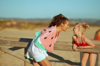 mutlu modern anne ve kızı deniz kıyısı eğleniyor akşam üzerinde mayo zaman. Anne ve kızı bir ahşap fence.kids eğlenceli ve sahilde tatil sırasında oynamak için aktif spor gibi yakın: