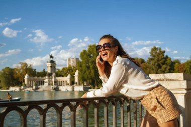 beyaz gömlek ve şort bir cep telefonu kullanarak El Retiro Park Madrid, İspanya şık kadın gülümsüyor. kadın aile ya da sevilen bir ve pay deneyim için Madrid gezisi hakkında söz. Mavi gökyüzü.