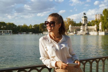 gülümseyen Smartphone için paylaşımı ve ağ veya sanal seyahat acentası yardım alma bilgileri kullanarak zarif kadın beyaz bluz ve Retiro Park Madrid, İspanya, şort. macera turizmi.