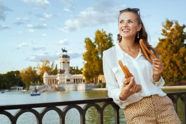 beyaz gömlek ve şort geleneksel İspanya churro yeme El Retiro Park Madrid, İspanya şık mutlu traveler kadın. churro - klasik İspanyol tatlı tedavi. beyaz kadın. Mavi gökyüzü. solo 